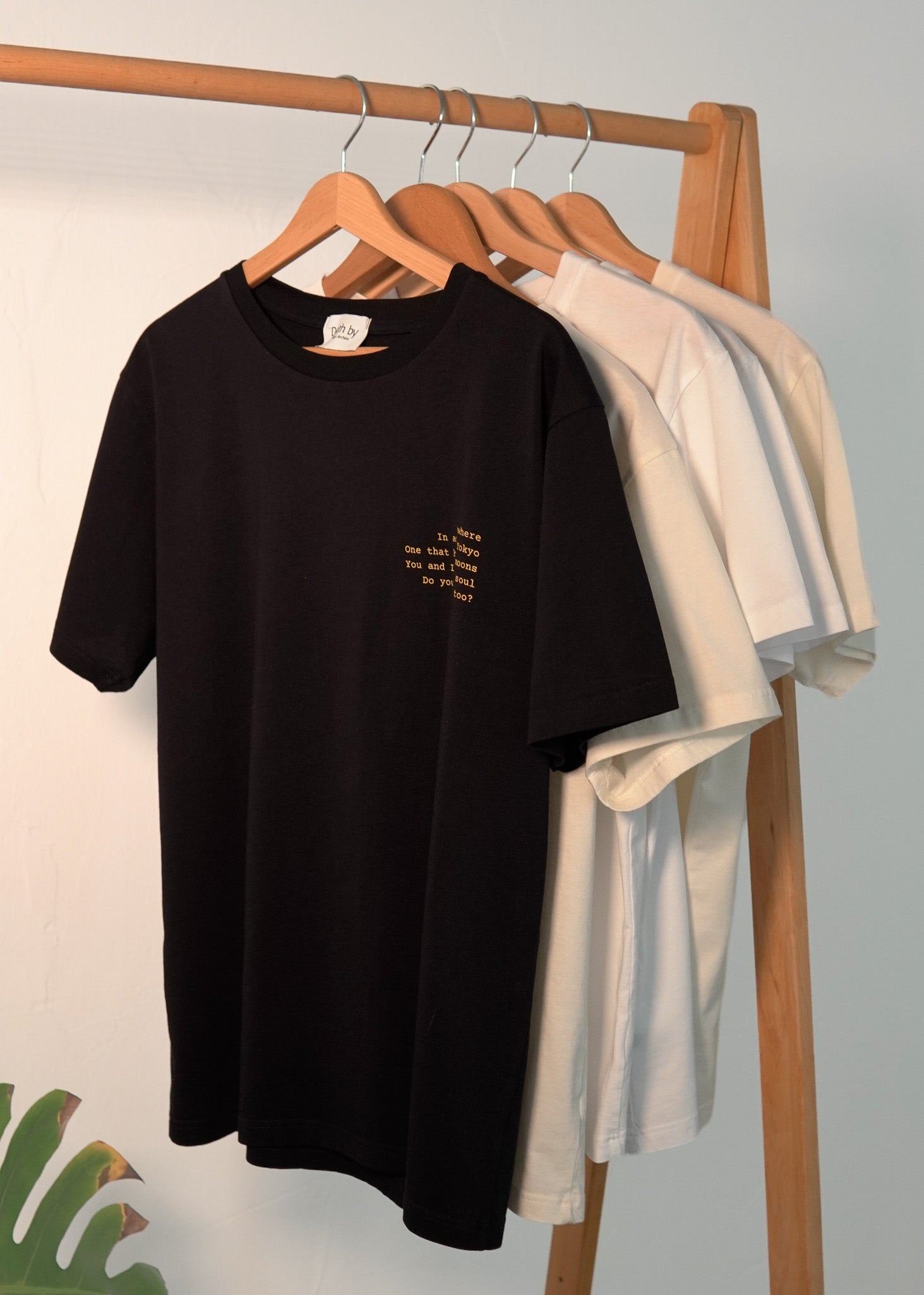 Black t-shirt with text on a wooden rack against a white wall
