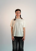 Person wearing a plain beige t-shirt and dark jeans against a light background