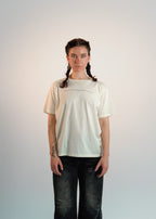 Person wearing a plain beige t-shirt and dark jeans against a light background