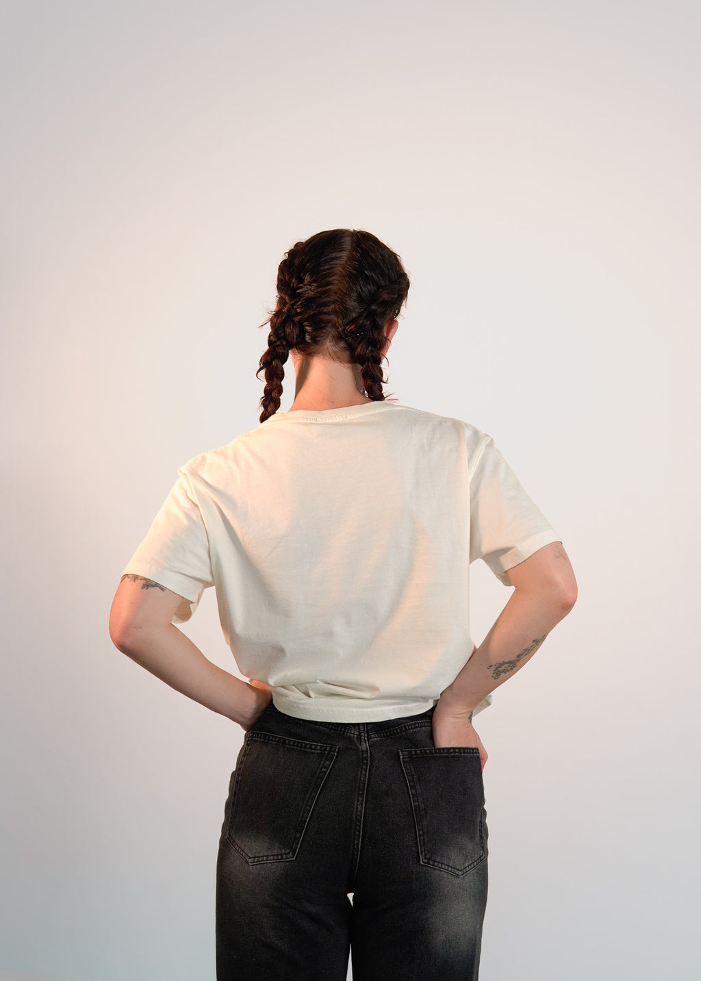 Person wearing a off white t-shirt and black pants against a plain background