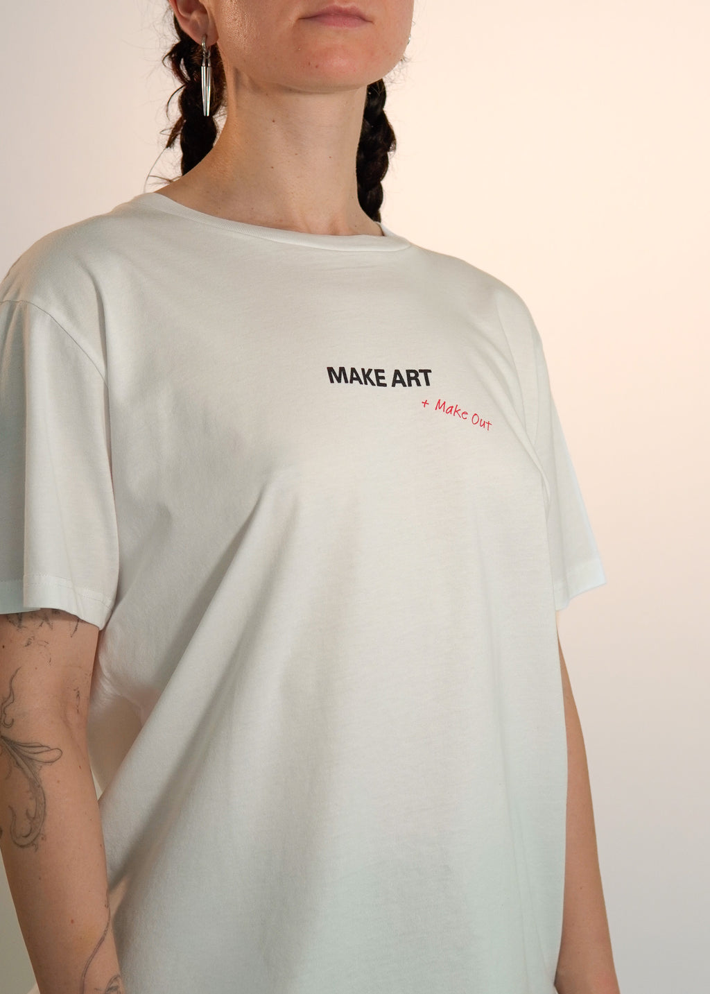 Person wearing a whiite t-shirt with 'MAKE ART' text on a plain background