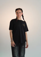 Person wearing a black t-shirt with a logo on a plain background