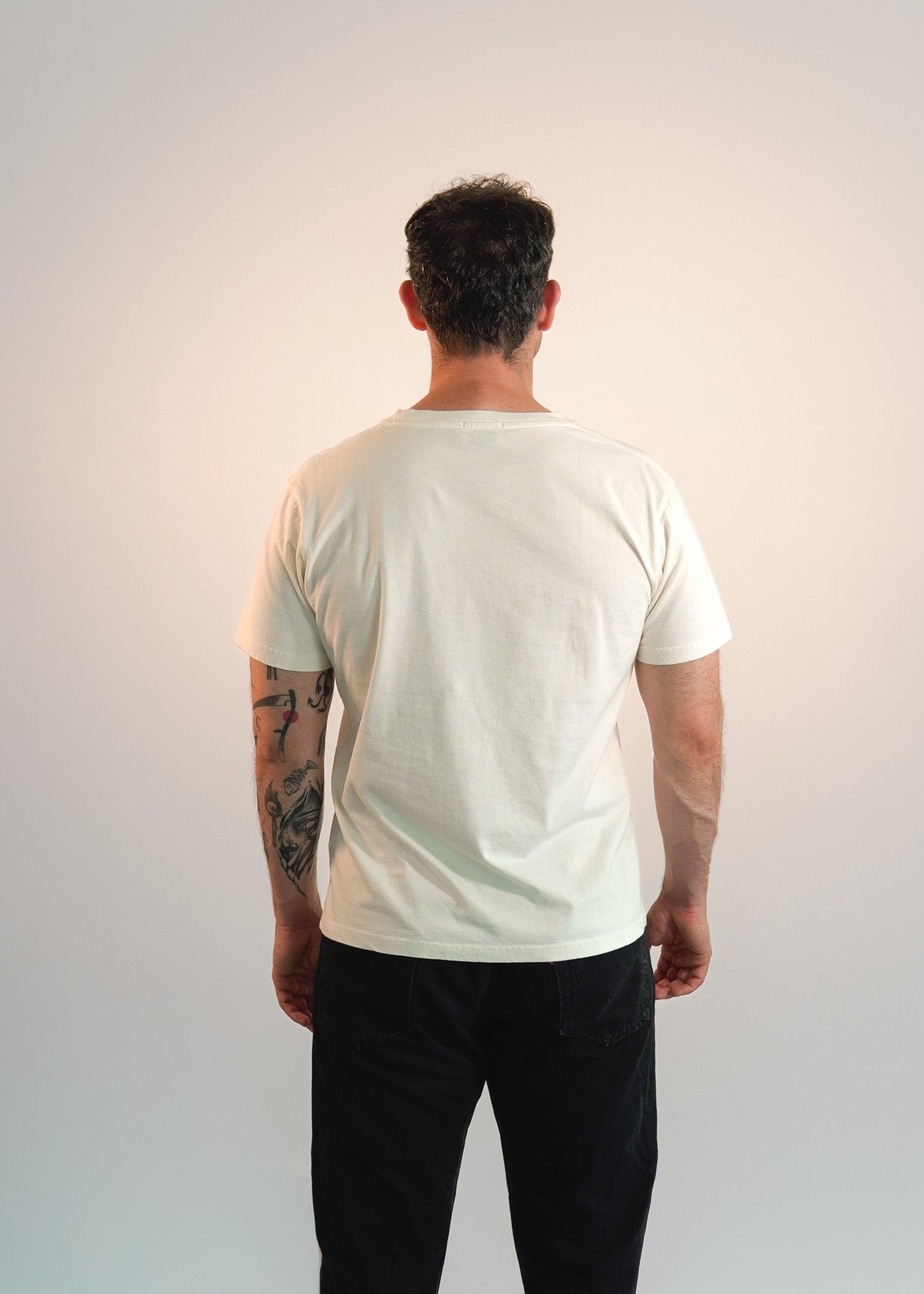 Man wearing a plain off-white t-shirt and black pants against a white background